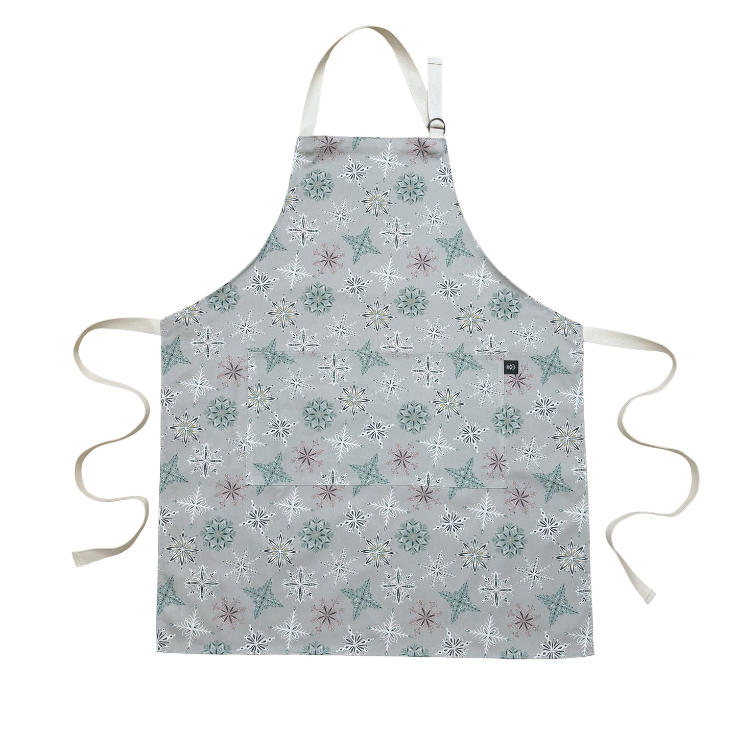 A grey snowflake apron laid flat on a white background.  It has Ecru cotton ties and adjustable cotton neck strap.