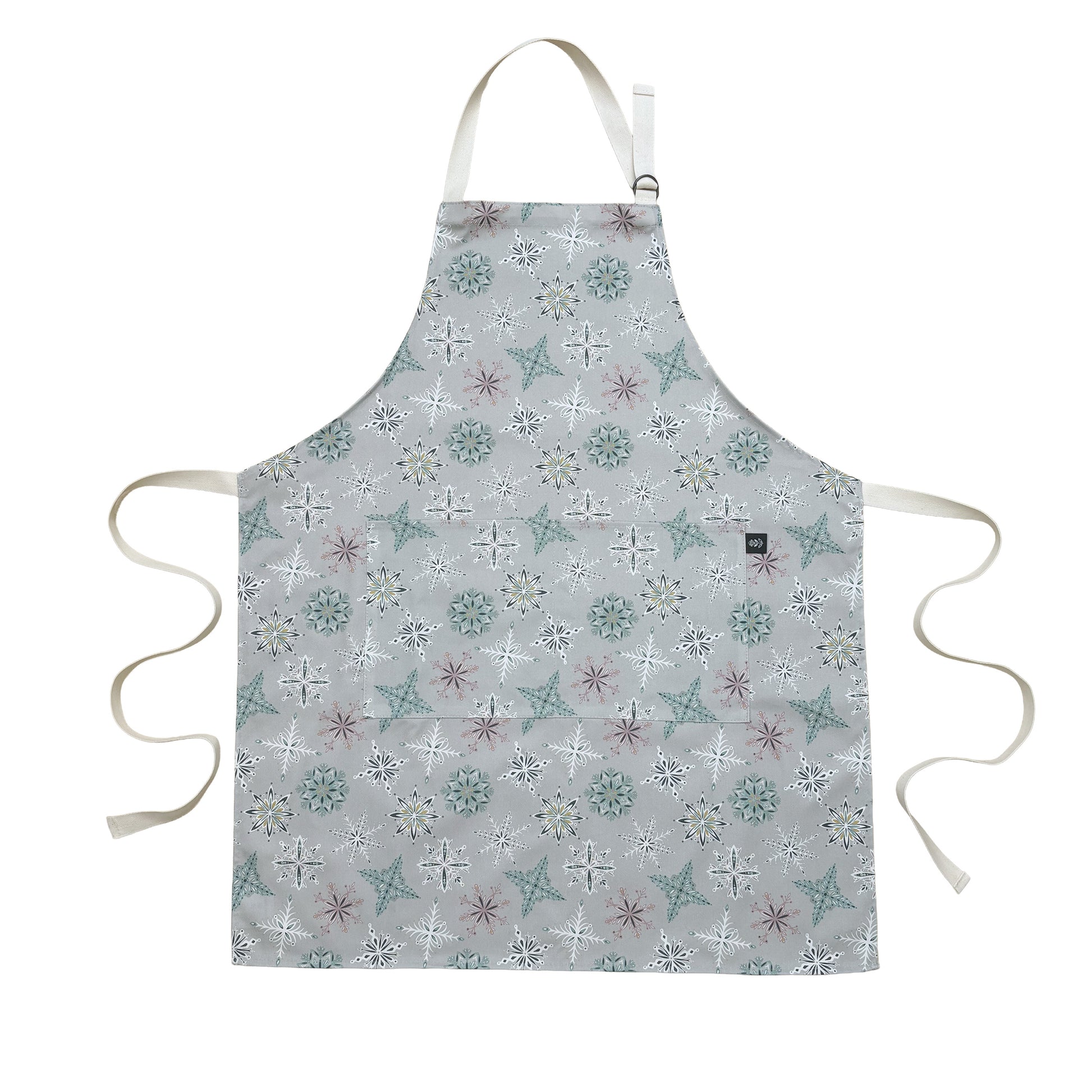 A grey snowflake apron laid flat on a white background.  It has Ecru cotton ties and adjustable cotton neck strap.