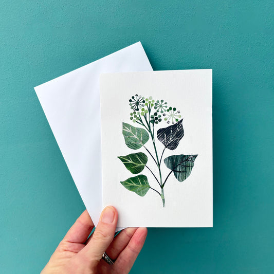 A hand is holding a textured greeting card featuring a collage of a Green Ivy Leaf and a white envelope against a Teal Wall.