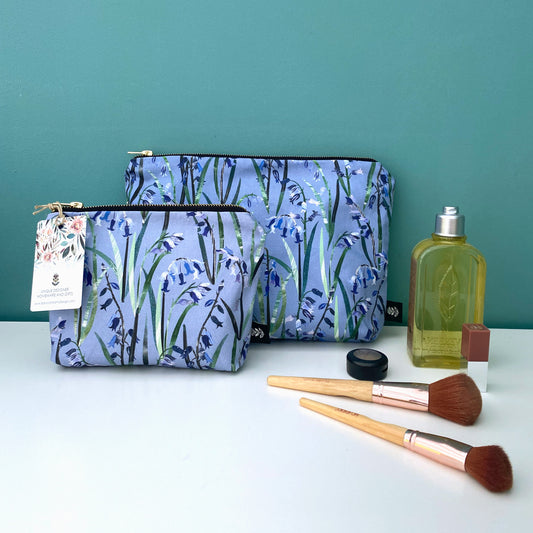 A Small Bluebells Wash Bag has been placed in front of a large Bluebell wash bag.  They are placed on a white shelf with a blue green background.