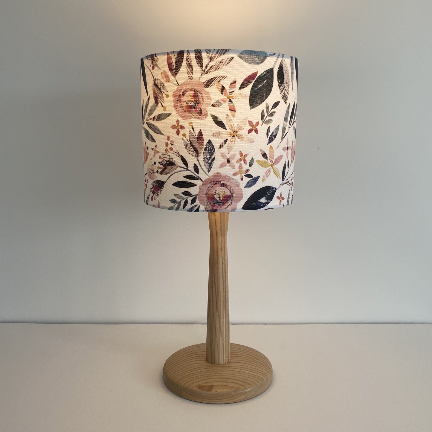 Small Summer Floral Lampshade on a wooden lamp base shown here with the light bulb on.