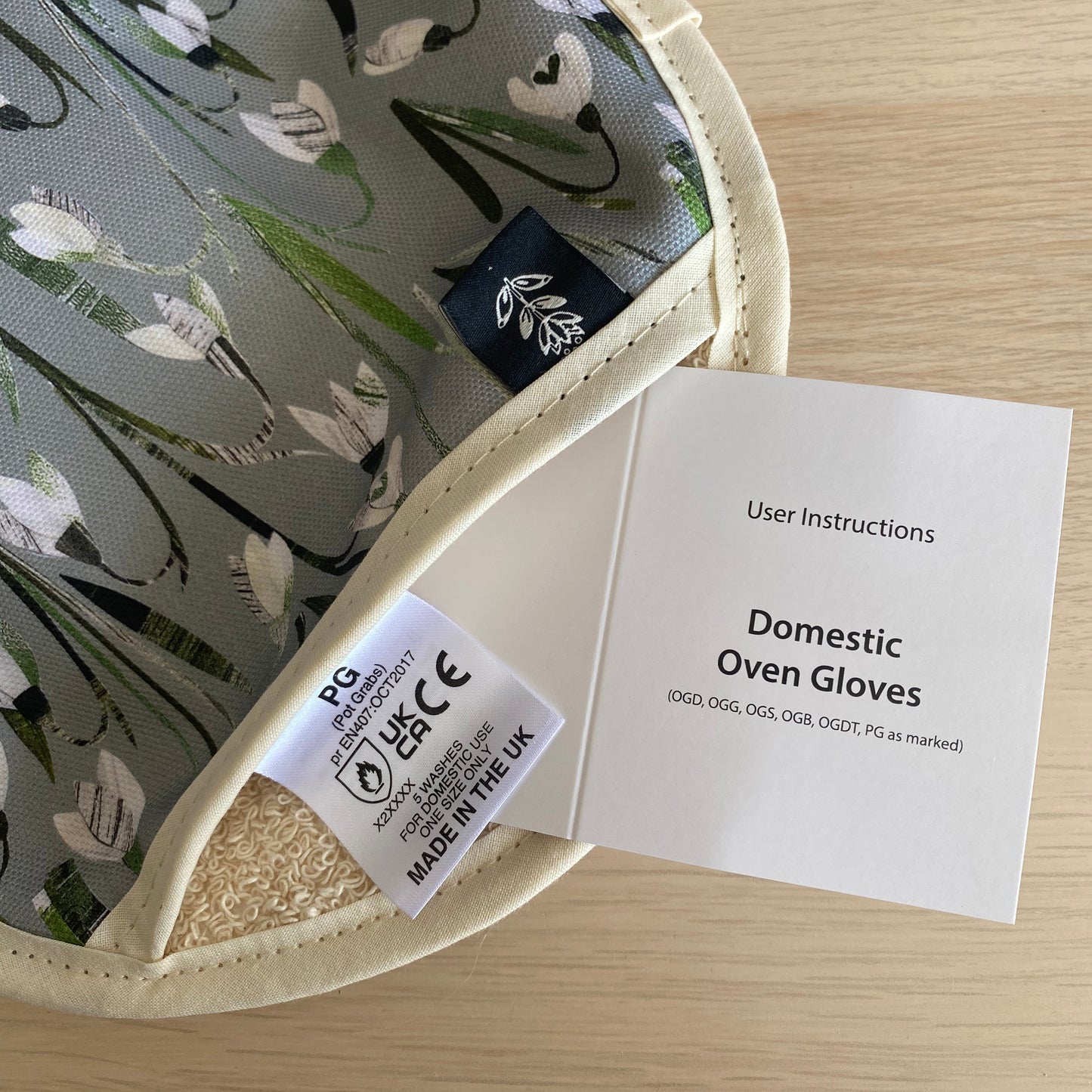 Close up of the Snowdrops Sing Oven Mitt showing the care label and user instructions.