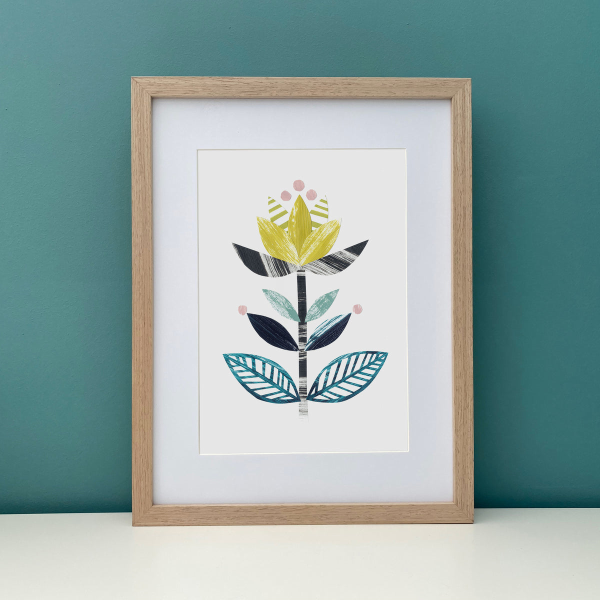 Framed artwork with a stylized leaf design on a teal wall.