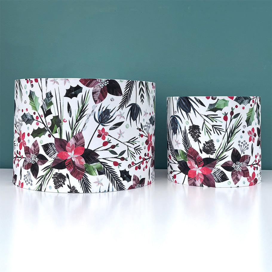 A medium and small sized Winter floral lampshades have been placed on a white shelf with a blue green background.