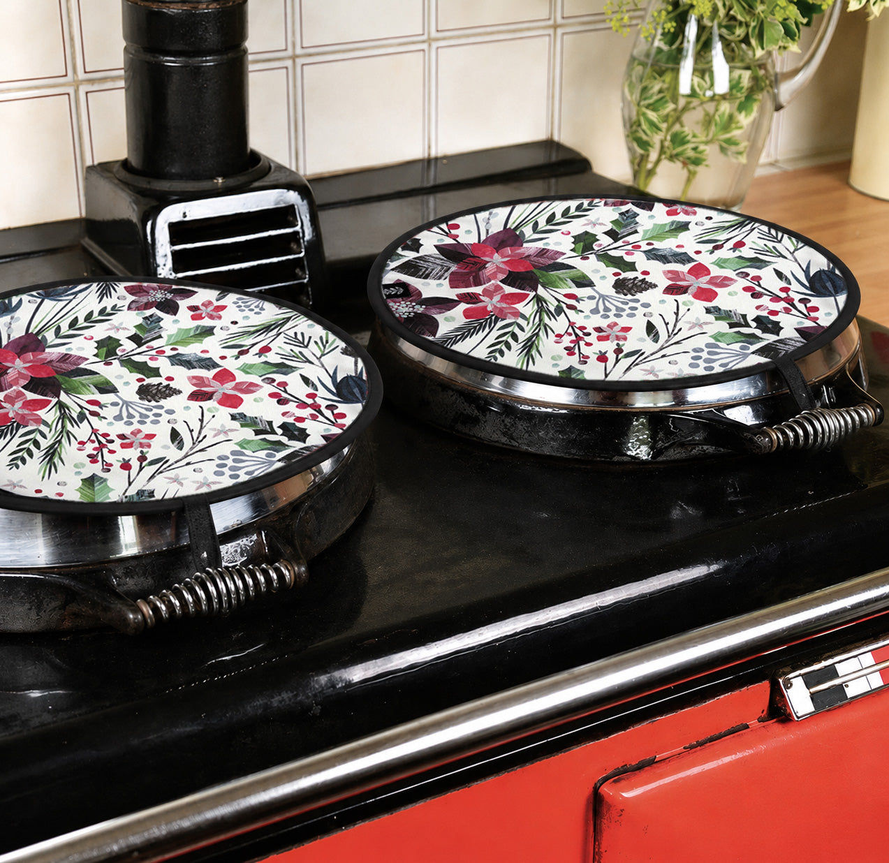 Two round Aga Covers with winter floral patterns on them have been placed on a red Aga with a black top.